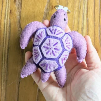 Main qui tient Lulu la tortue mauve, porte-clé en feutrine fait-main par l'Atelier Jocha